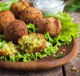 Zdjęcie przedstawia udekorowany sałatą drewniany talerz, na nim kilka falafli