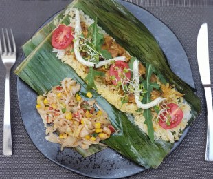 Zdjęcie przedstawia potrawę na talerzu, Tempeh z duszonym po tajsku porem, grilowany w liściu bananowca z ryżem, podany z surówką